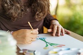 person painting flowers with a brush on paper using watercolors in a natural setting seven colors used in artwork