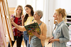 four women engaged in a painting class working together on art projects inspired by creativity and teamwork for six artists