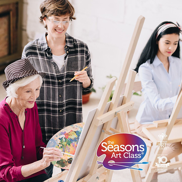 three women participating in an art class painting on easels with colorful palettes and art supplies